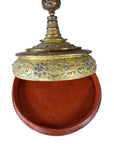 Close-up of round red lacquered Burmese offering bowl with gilt, jewel-studded lid, ornate mica inlay, partially open.