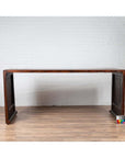 Dark wood Burmese vintage waterfall console table with scrolling feet on a wood floor against a white brick wall.