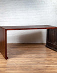 Dark wood Burmese vintage waterfall console table with scrolling feet on a wooden floor against a white brick wall.