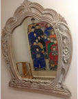 Brown carved wooden mirror reflecting portrait of people in traditional attire, wooden chair visible in background.