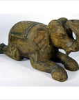 Close-up of hand-carved wooden elephant figurine from Chiang Mai, kneeling with trunk raised, decorative patterns visible.