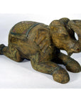 Close-up of hand-carved wooden elephant figurine from Chiang Mai, kneeling with trunk raised, decorative patterns visible.