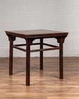 Brown elmwood Chinese 19th c. center hall table with Ming Dynasty stone inset by a white brick wall on wood flooring.