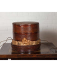 Brown wood tiered food basket with stacking sections on dark table, white brick wall background, 19th century Chinese style.