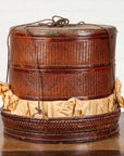 Brown wood Chinese tiered food basket with rope handles, lid, stacking sections, and crumpled paper at base.