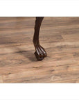 Close-up of dark wood cabriole leg with carved animal paw detail on light floor, classic antique table style.