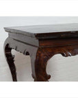 Black lacquered wood hall table with cabriole legs, set indoors against a light brick wall.