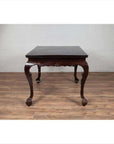 Black lacquered wood hall table with cabriole legs on wood floor against white brick wall indoors.