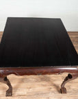 Black lacquered wood center hall table with cabriole legs on a wooden floor against a white wall indoors.