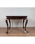 Black lacquered wood center hall table with cabriole legs on a wood floor next to a white brick wall indoors.