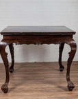 Black lacquered wood hall table with cabriole legs, placed on wooden floor next to a white brick wall indoors.