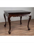 Black lacquered wood hall table with cabriole legs on a wood floor against a white brick wall indoors.