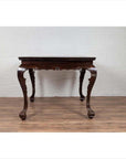 Black lacquered wood hall table with cabriole legs, positioned on a wooden floor against a white brick wall indoors.