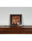 Red giltwood Chinese antique floral architectural panel on a wooden table, white brick wall background.