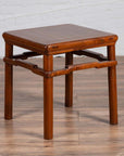 Brown wood Chinese Ming style side table with humpback stretcher on wood floor by white brick wall.