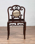 Dark rosewood antique side chair with open fretwork and marble medallion, on a wooden floor.