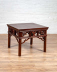 Dark wood Chinese antique side table with open fretwork design on wooden floor against white brick wall.