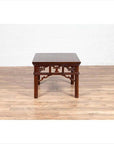 Dark wood Chinese antique side table with open fretwork design on light wood floor, white wall background.