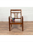 Brown elmwood Chinese Art Deco armchair with geometric backrest, color card on seat, on wood floor, white brick wall.