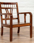 Brown elmwood Chinese Art Deco armchair with pierced curved back, positioned by a white brick wall on wood flooring.
