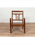 Brown elmwood Chinese Art Deco 1950s armchair with pierced and curved design on wooden floor, white brick wall background.