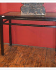 Black Chinese console table with straight legs, set against a red wall and wooden floor.