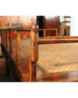 Close-up of a brown wood Chinese daybed with woven cane surface and simple railings in a Shanxi-inspired indoor setting.