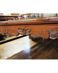 Close-up of dark wood Chinese daybed with carved floral and leaf patterns along the side, shown on a wooden floor.