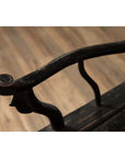 Close-up of dark patina Chinese elmwood chair armrest with curved carvings, blurred floor background.