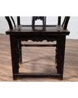 Dark-finish elmwood chair on wooden floor with white brick wall background.