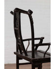 Dark patina elmwood chair with curved backrest, placed indoors against a white brick wall.