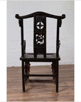 Dark wood chair with ornate backrest, on wooden floor, white wall background.