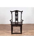 Dark patina elmwood scholar's chair with carvings on wood floor against white brick wall indoors.