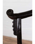 Close-up of dark patina elmwood chair scroll armrest, light background.