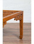Close-up of a brown elmwood coffee table leg with horse-hoof feet and open fretwork, indoors against a white wall.