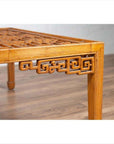 Close-up of brown elmwood square coffee table with open fretwork and horse-hoof legs on a wooden floor.