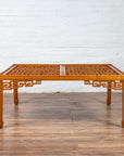 Brown elmwood square coffee table with open fretwork and horse-hoof legs on wooden floor by white brick wall indoors.