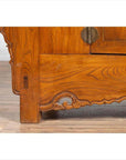 Close-up of brown elmwood two-door low cabinet with everted flanges, scrolls, and visible hinge.