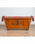 Brown elmwood two-door low kang cabinet with everted flanges, scroll details, round metal handles, red cloth on top.