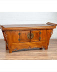 Brown elmwood low cabinet with two doors, everted flanges and scrolls, against white brick wall on wood floor.