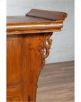 Close-up of a brown elmwood two-door low cabinet with everted flanges and scrolls on a wooden floor.