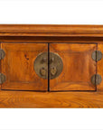 Close-up of brown elmwood cabinet doors with circular brass hardware and carved floral scrolls.