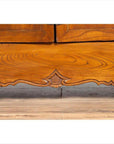 Close-up of brown elmwood two-door low cabinet with everted flanges and scrolls on a wood floor.