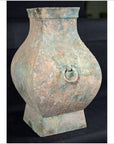 Weathered brown ceramic Han Dynasty hu vessel with square base and ring handle, close-up on black background.