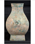 Weathered bronze Chinese Han Dynasty Hu vessel with ring handle and rectangular base, on black background.