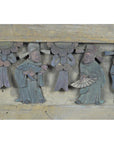 Brown wood plaque with hand-carved three robed figures holding fans, floral details above, close-up view.
