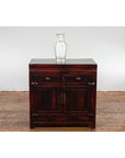 Reddish black lacquered wood side cabinet, Late Qing Dynasty 1900s, on wooden floor with glass vase beside it.