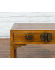 Close-up of a brown elm wood Chinese Late Qing Dynasty desk with two drawers and ornate brass hardware, white brick wall background.