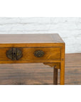 Brown elm wood desk with two drawers and ornate brass hardware, Late Qing Dynasty, on wooden floor by white brick wall.