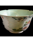 Close-up of Chinese porcelain bowl with scalloped rim, painted landscapes, cranes, and light green interior.
